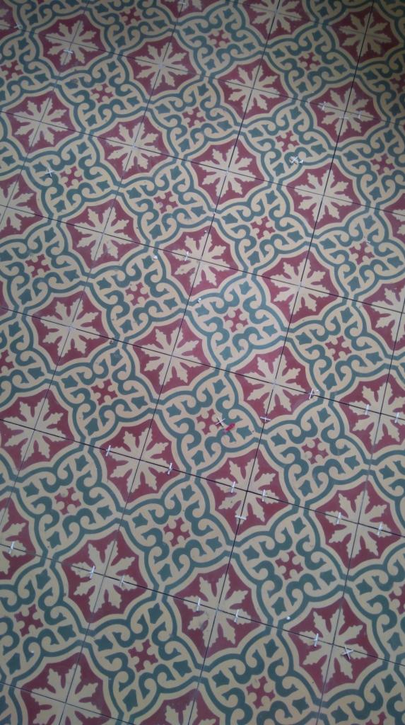 Wzorzysta podłoga z płytek w odcieniach czerwieni, zieleni i beżu, ułożona w geometryczny motyw. Widoczne krzyżyki dystansowe między płytkami.