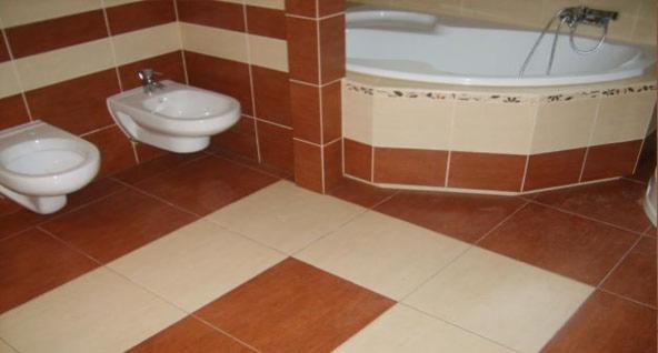 Wykończona łazienka z brązowo-beżowymi płytkami, z widoczną wanną obudowaną płytkami, bidetem i toaletą.