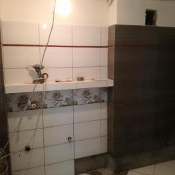 Private - Układanie płytek w łazience: białe i brązowe płytki, narzędzia glazurnicze na półce, widoczne przewody elektryczne i niedokończone fugowanie.