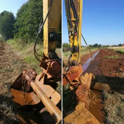 Żółta koparka z brudnym, zakleszczonym korzeniem w łyżce, pracująca przy rowie melioracyjnym na polu w słoneczny dzień.