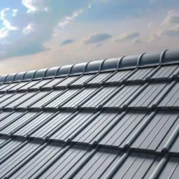 Szary dach pokryty metalową dachówką modułową z widocznym niebem i chmurami w tle.