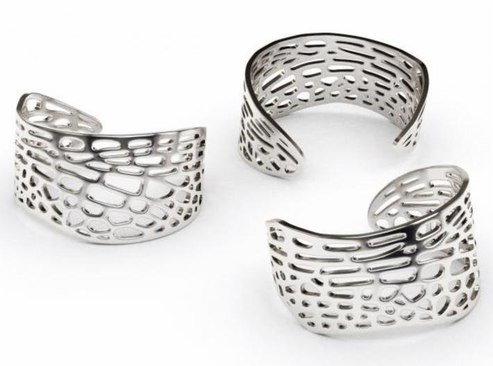 Trzy srebrne bransoletki typu cuff z ażurowym wzorem na białym tle, prezentujące różne perspektywy projektu.