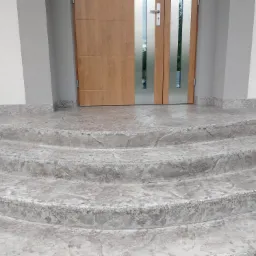 Czterostopniowe schody wejściowe z betonu stemplowanego, imitującego naturalny kamień, prowadzące do nowoczesnych drzwi z przeszkleniami.