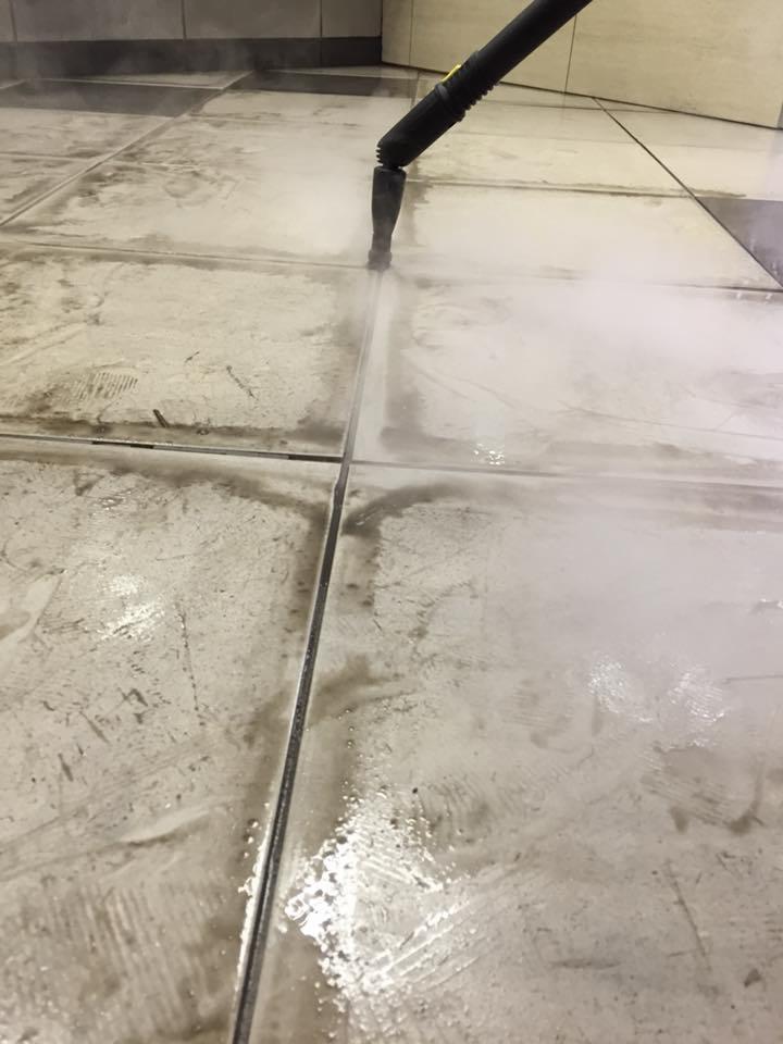 Czyszczenie fug na podłodze z płytek za pomocą parownicy, widoczny efekt czyszczenia i para wydobywająca się z dyszy urządzenia.