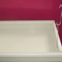 Wysuwana szuflada w kolorze złamanej bieli, przymocowana do regału za pomocą metalowych zawieszek, na tle ściany w kolorze fuksji.