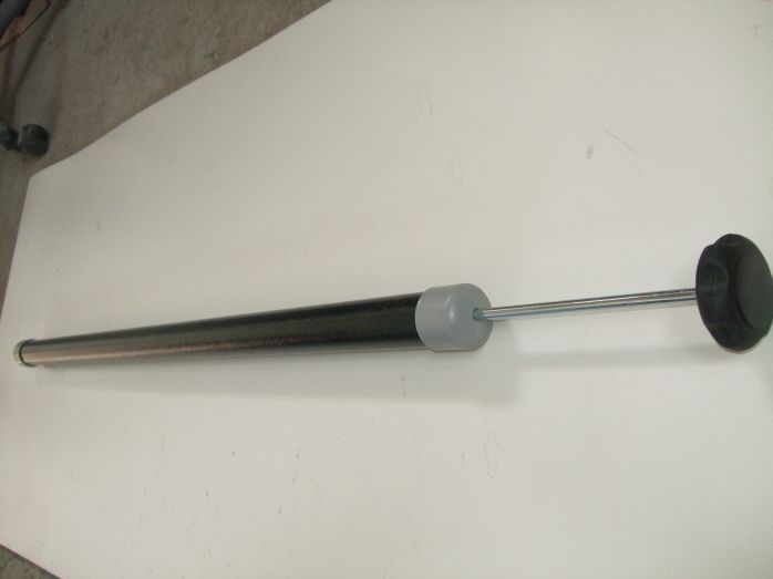 Czarny amortyzator gazowy z szarymi elementami mocującymi i tłokiem, leżący na białej powierzchni.