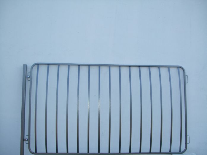 Szary panel płotowy z pionowymi prętami na tle jasnej ściany, widoczne elementy mocujące.