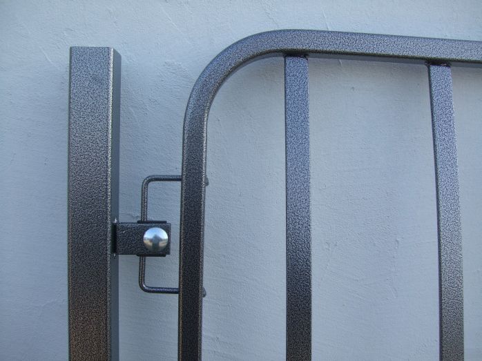 Metalowy panel ogrodzeniowy z widocznym mocowaniem i fakturą w kolorze szaro-srebrnym na tle jasnej ściany.