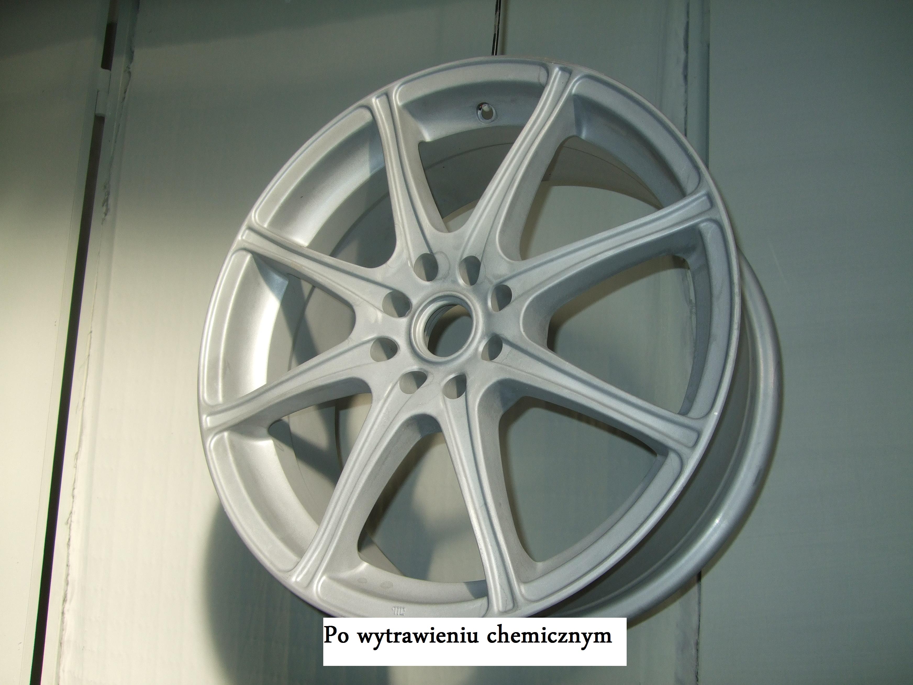 Srebrna felga aluminiowa z ośmioma ramionami, zawieszona na haku, po procesie trawienia chemicznego.
