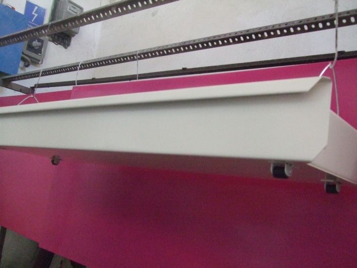 Biała szuflada pod regał z różowym tłem, zawieszona na metalowych haczykach.