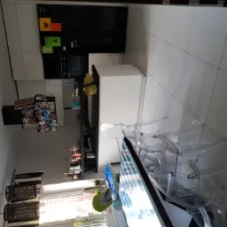 Nowoczesna, biała kuchnia z czarnymi akcentami, wyposażona w przezroczyste krzesła i dziecięcy fotelik, widziana z perspektywy podłogi, z dekoracjami na ścianach i butelkami na półkach.