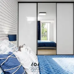 Sypialnia z białymi cegłami na ścianie, łóżkiem z niebieską pościelą i szafą przesuwną z lustrem odbijającym fragment pokoju z oknem.