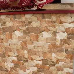 Ściana wykończona płytkami imitującymi kamień w odcieniach beżu i brązu, z widocznym fragmentem czerwonej markizy u góry.