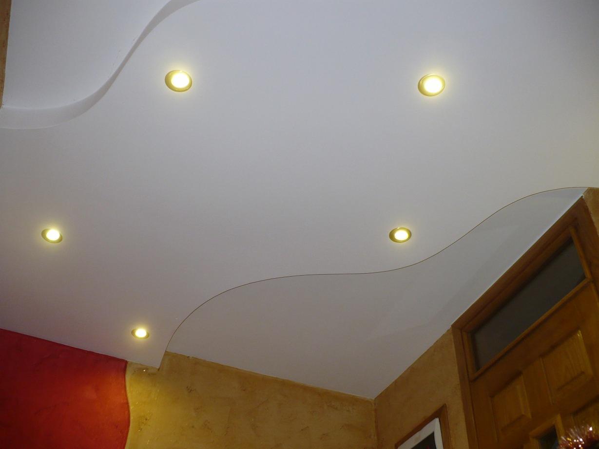 Biały sufit napinany z falistym wzorem i sześcioma wbudowanymi punktowymi lampami LED, widok z dołu, ściany w kolorze czerwonym i ochry.