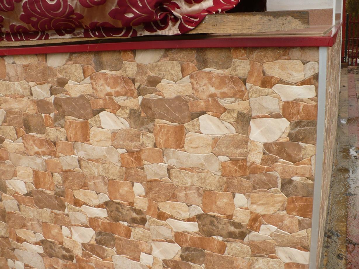 Ściana wykończona płytkami imitującymi kamień w odcieniach beżu i brązu, z widocznym fragmentem czerwonej markizy u góry.