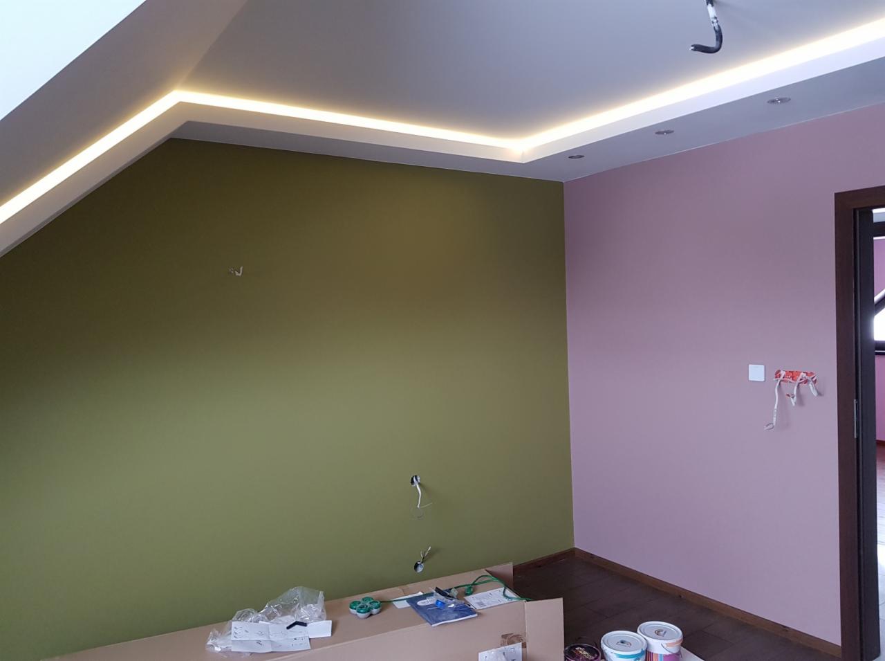 Pokój po remoncie z dwiema ścianami w odmiennych kolorach (oliwkowy i różowy), z podwieszanym sufitem z oświetleniem LED oraz widocznymi puszkami farb i narzędziami malarskimi.