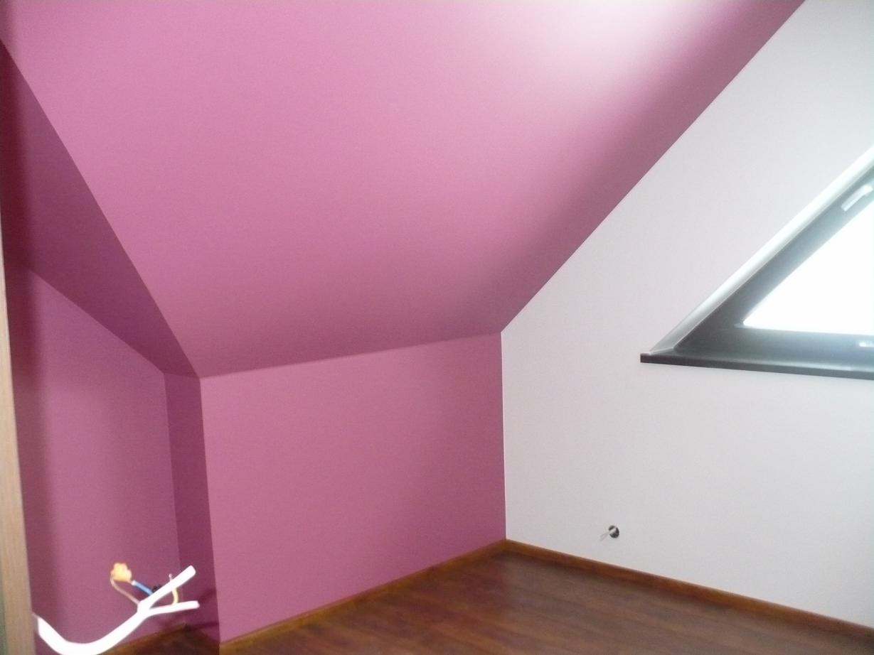Poddasze po remoncie: ściany pomalowane na różowo, skośny sufit i trójkątne okno dachowe, widoczne wystające kable elektryczne.