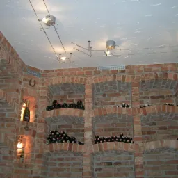 Piwnica z cegły z wnękami wypełnionymi butelkami wina, oświetlona systemem szynowym z reflektorami punktowymi