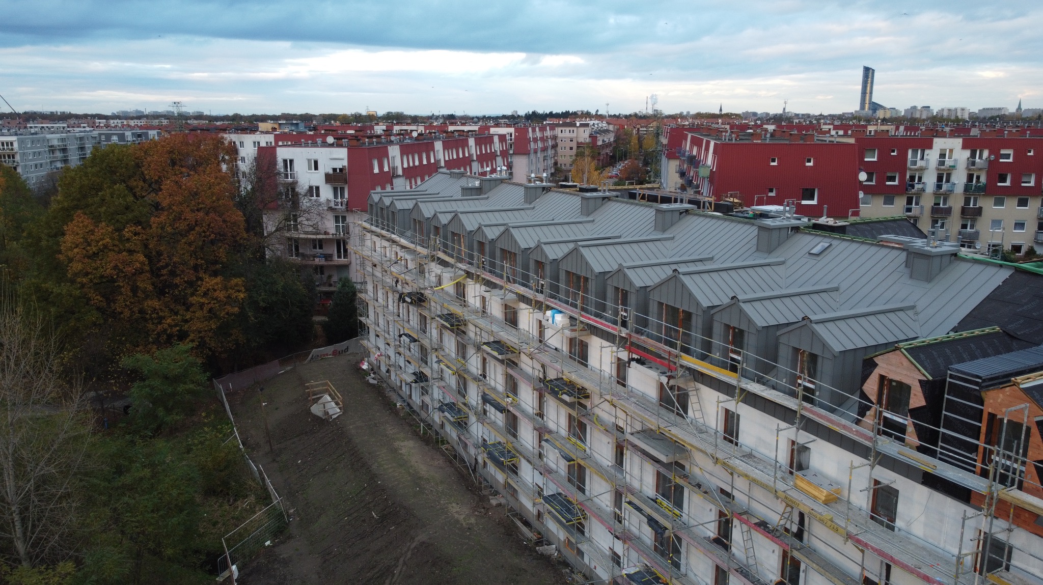 Kąty Wrocławskie: Nowe, szare pokrycie dachowe na wielopiętrowym budynku w trakcie budowy, z widocznymi rusztowaniami i elementami konstrukcyjnymi.