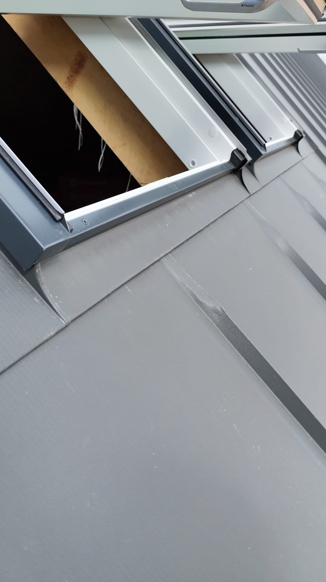 Szare pokrycie dachowe z zamontowanym oknem dachowym Fakro, widoczny fragment więźby dachowej. Ujęcie z bliska, skupione na detalu montażu.