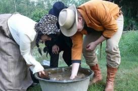 Trzy osoby w strojach stylizowanych na western myją ręce w metalowej balii na zewnątrz, w tle widoczna zieleń.