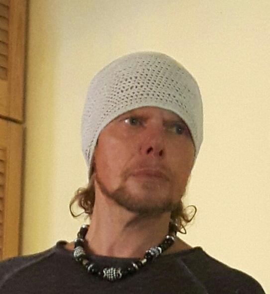 Mężczyzna w ażurowym czepku kąpielowym i naszyjniku z czarnych koralików, spoglądający w górę.