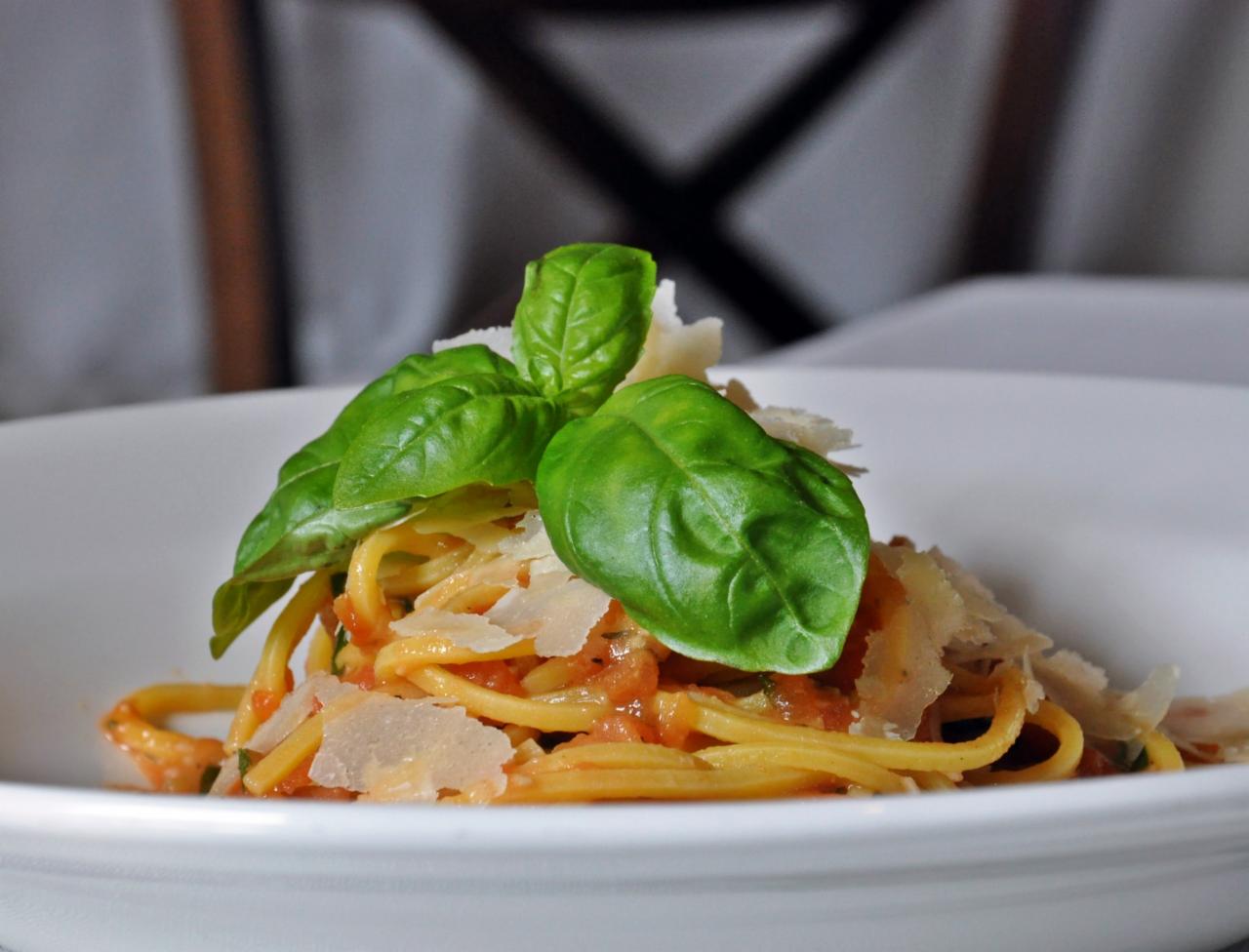 Porcja spaghetti z sosem pomidorowym, posypana płatkami parmezanu i świeżą bazylią na białym talerzu, widok z bliska.