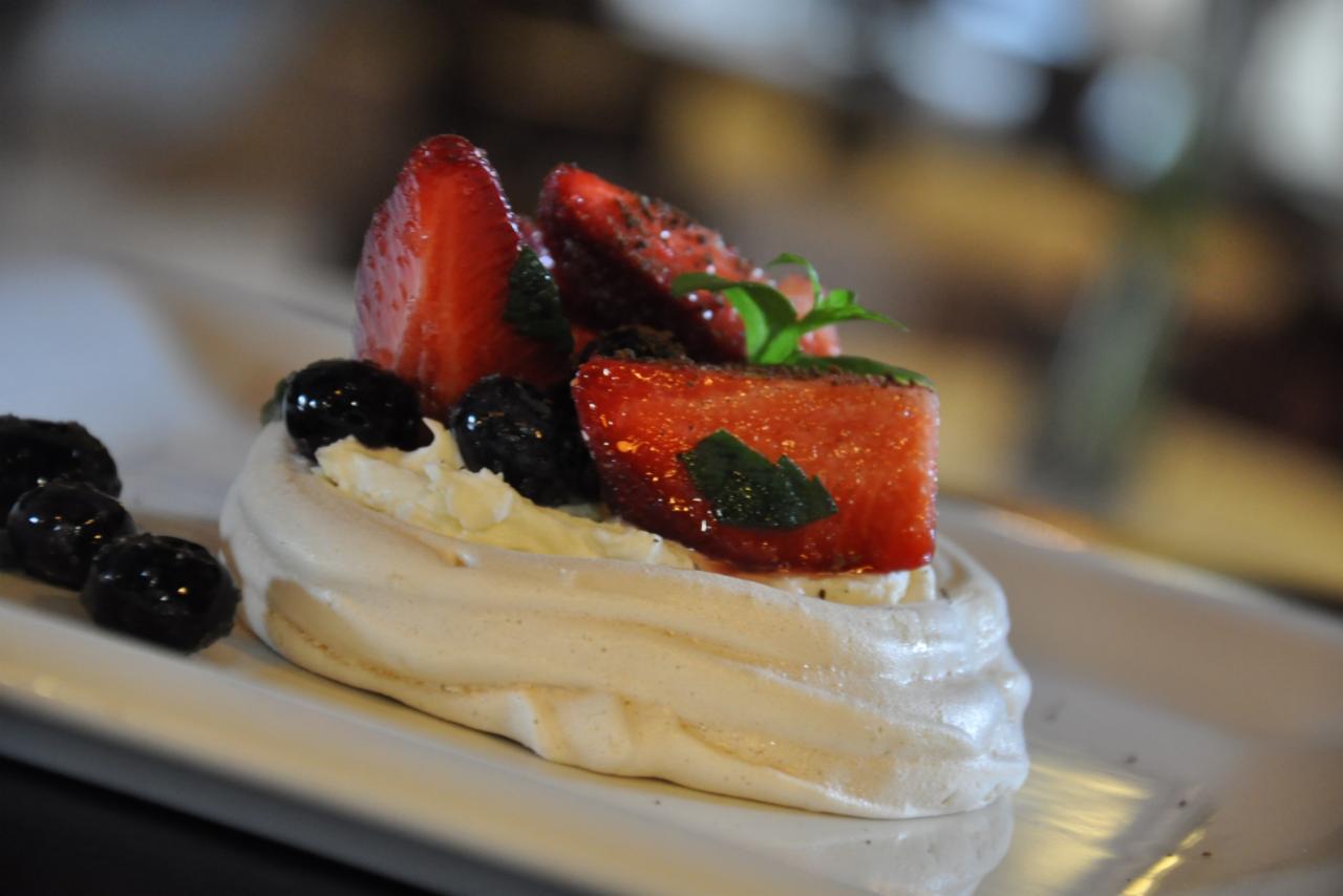 Delikatna beza z bitą śmietaną, świeżymi truskawkami, borówkami i listkami mięty na białym talerzu.