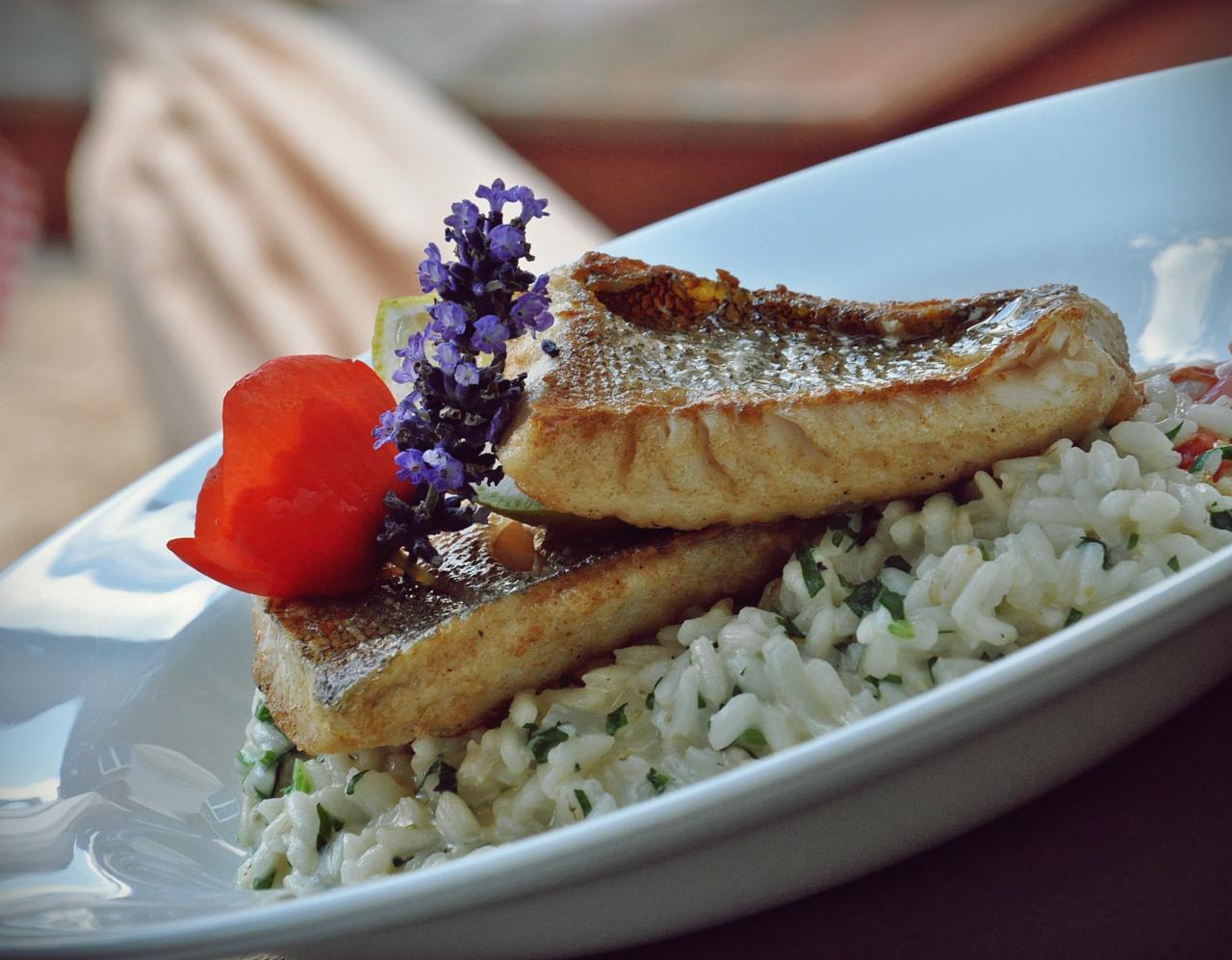 Elegancko podane danie rybne z ryżem i dekoracjami kwiatowymi na białym talerzu, serwowane w restauracji w Zielonej Górze.