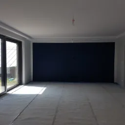 Pusty pokój z przygotowanym podłożem pod panele, widoczne okno przesuwne z widokiem na ogród i granatowa ściana.