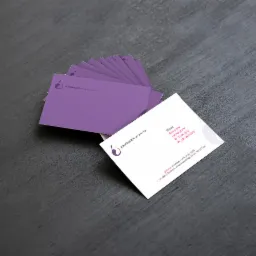 Stos fioletowych i białych wizytówek z logo i danymi kontaktowymi firmy Paulinablumkowska, specjalizującej się w masażach, ułożony na ciemnoszarym tle.