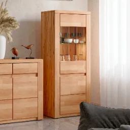 Drewniany kredens z przeszkloną witryną, na blacie komody dekoracje: biały wazon z suszem i drewniane figurki ptaków, na ścianie obrazek w ramie, jasne wnętrze.