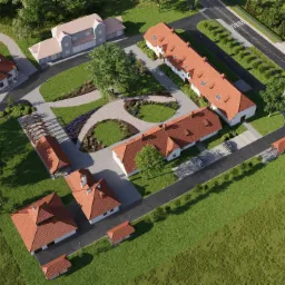 Widok z lotu ptaka na kompleks budynków z czerwonymi dachami, otoczonych zielenią, ścieżkami i drogami dojazdowymi.