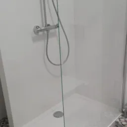 Nowoczesna kabina prysznicowa z białym brodzikiem, chromowaną armaturą i szklaną ścianką, wykończona płytkami podłogowymi w geometryczny wzór.