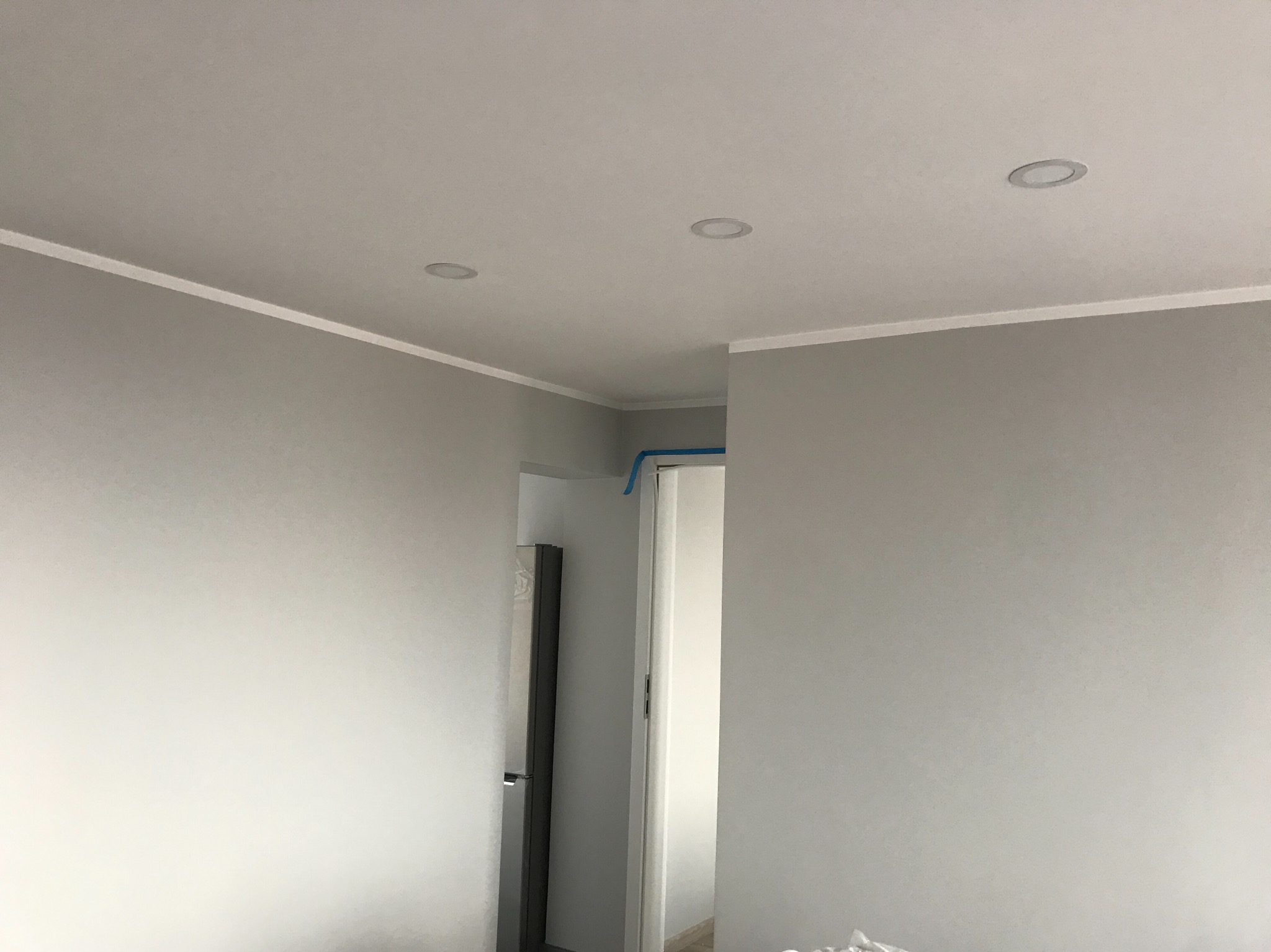 Wnętrze pomalowane na szaro z zamontowanymi listwami przysufitowymi i oświetleniem punktowym; w tle widoczne otwarte drzwi do innego pomieszczenia.