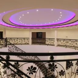 Wielopoziomowe wnętrze z czarnymi balustradami o motywie roślinnym i okrągłym sufitem z oświetleniem LED w kolorze fioletowym.