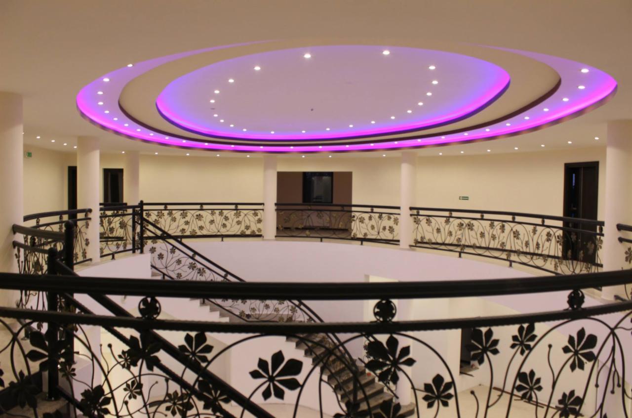 Wielopoziomowe wnętrze z czarnymi balustradami o motywie roślinnym i okrągłym sufitem z oświetleniem LED w kolorze fioletowym.