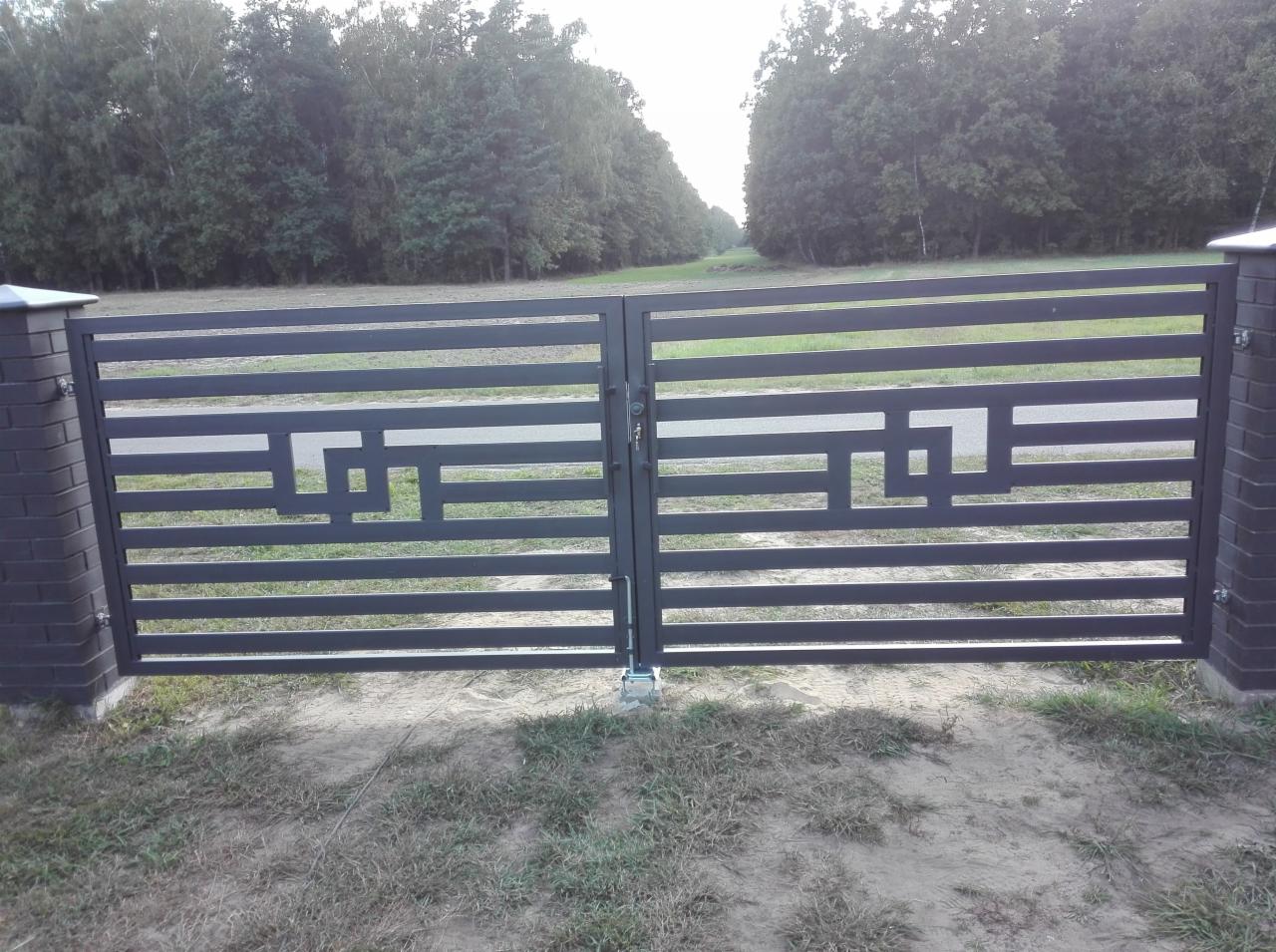 Nowoczesna, metalowa brama wjazdowa z poziomymi profilami i geometrycznym wzorem, osadzona na ceglanych słupkach z betonowymi daszkami, na tle zieleni.