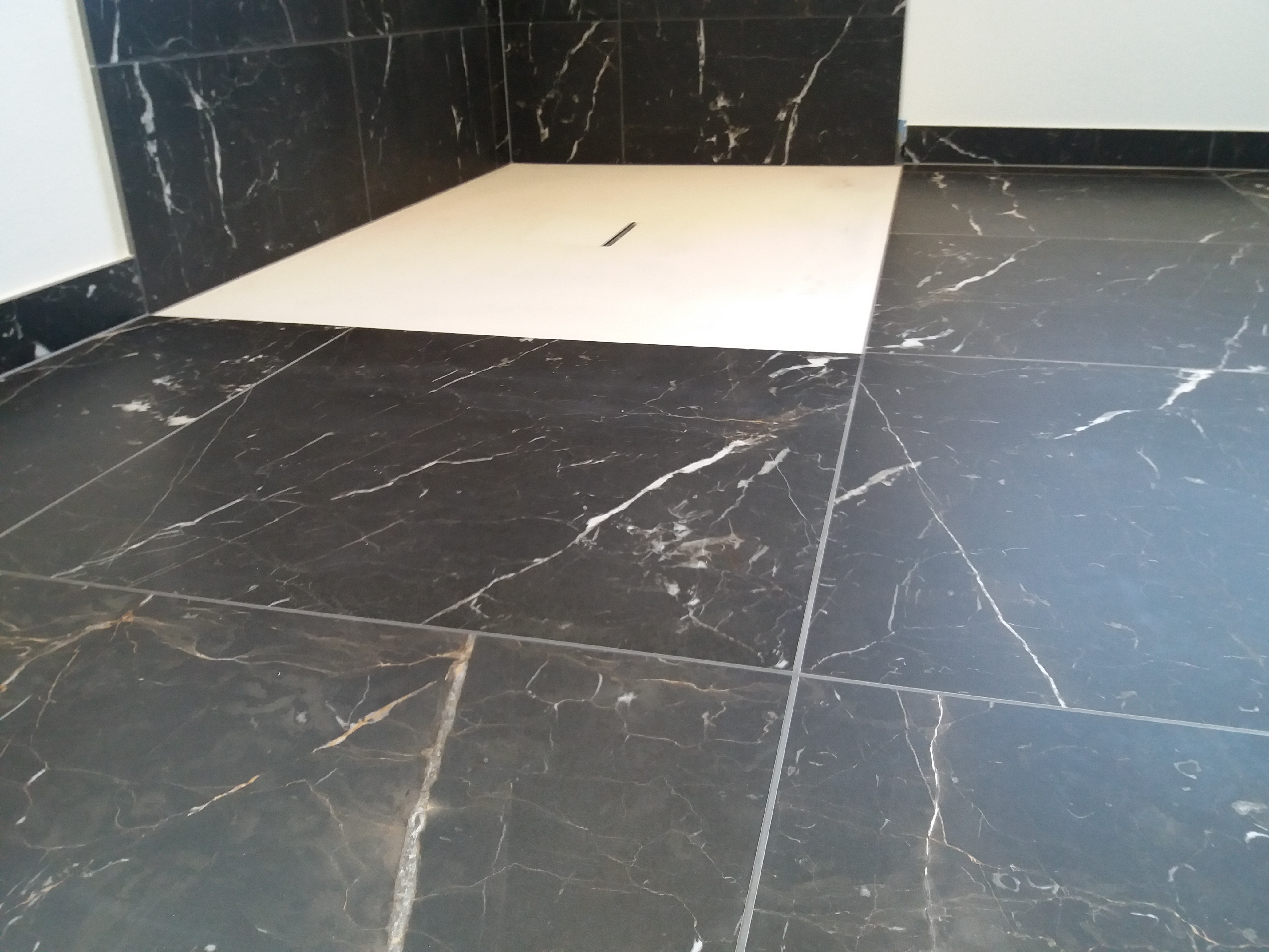 Czarne marmurowe płytki podłogowe i ścienne w łazience z białym brodzikiem z odpływem liniowym.