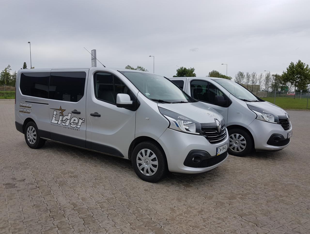 Dwa srebrne busy Renault Trafic zaparkowane na brukowanym placu, z logo 'Lider Transport Autokarowy' na boku pierwszego pojazdu.