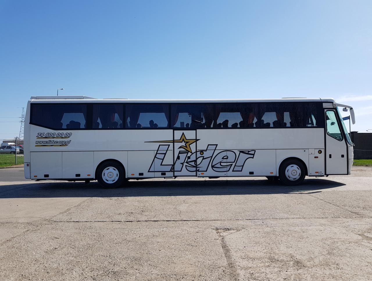 Biały autokar firmy transportowej ze Świdnicy, z dużym logo 'Lider' z gwiazdą, zaparkowany na betonowym placu w słoneczny dzień.