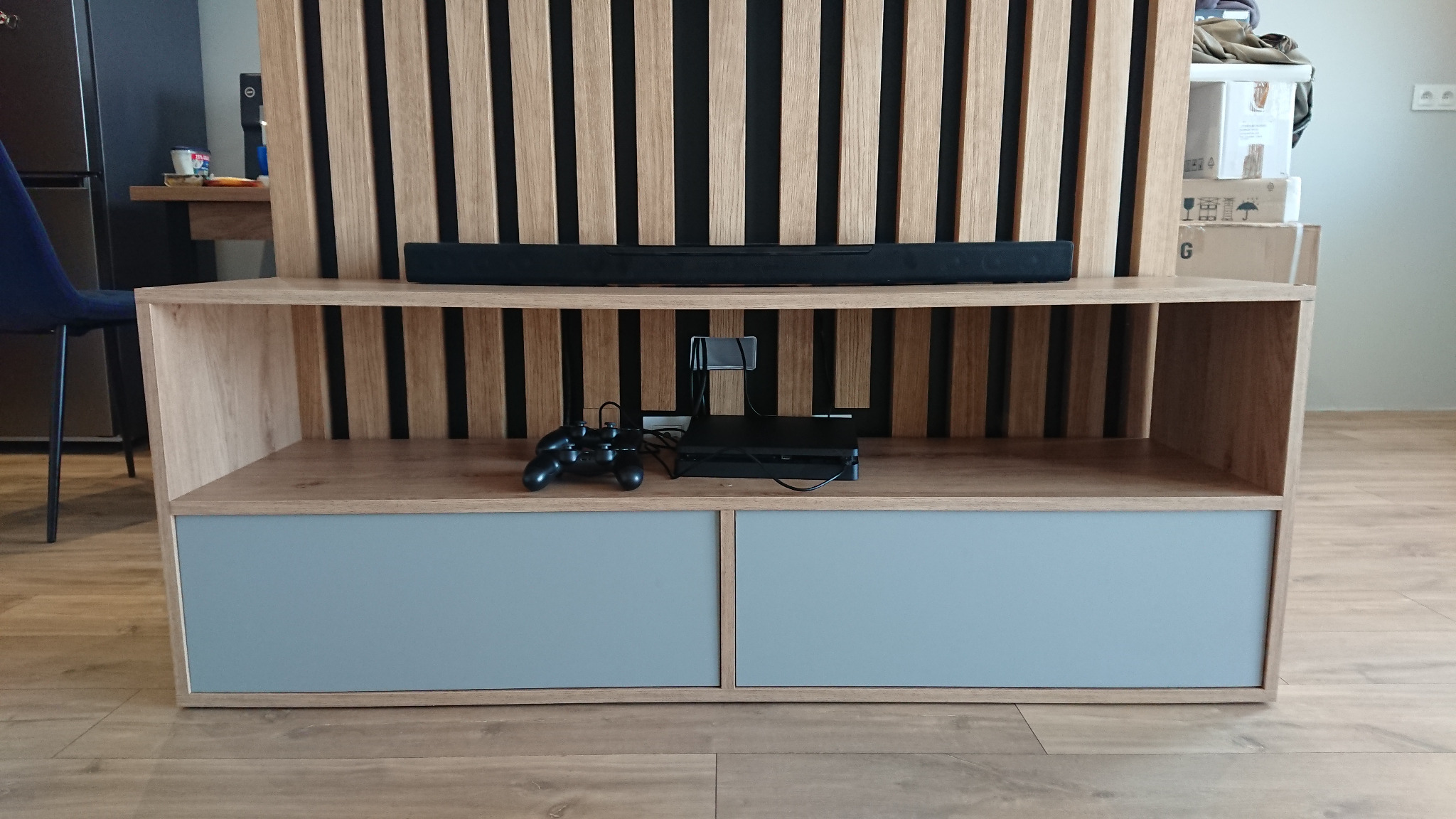 Drewniana szafka RTV z lamelami w tle, wykonana na wymiar w Krotoszynie, na półce konsola do gier.