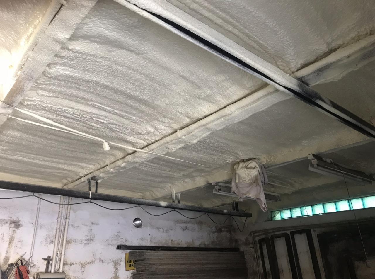 Poddasze ocieplone pianką PUR, widoczne rury instalacyjne i fragment ściany z widocznymi śladami zabrudzeń, oświetlenie halogenowe