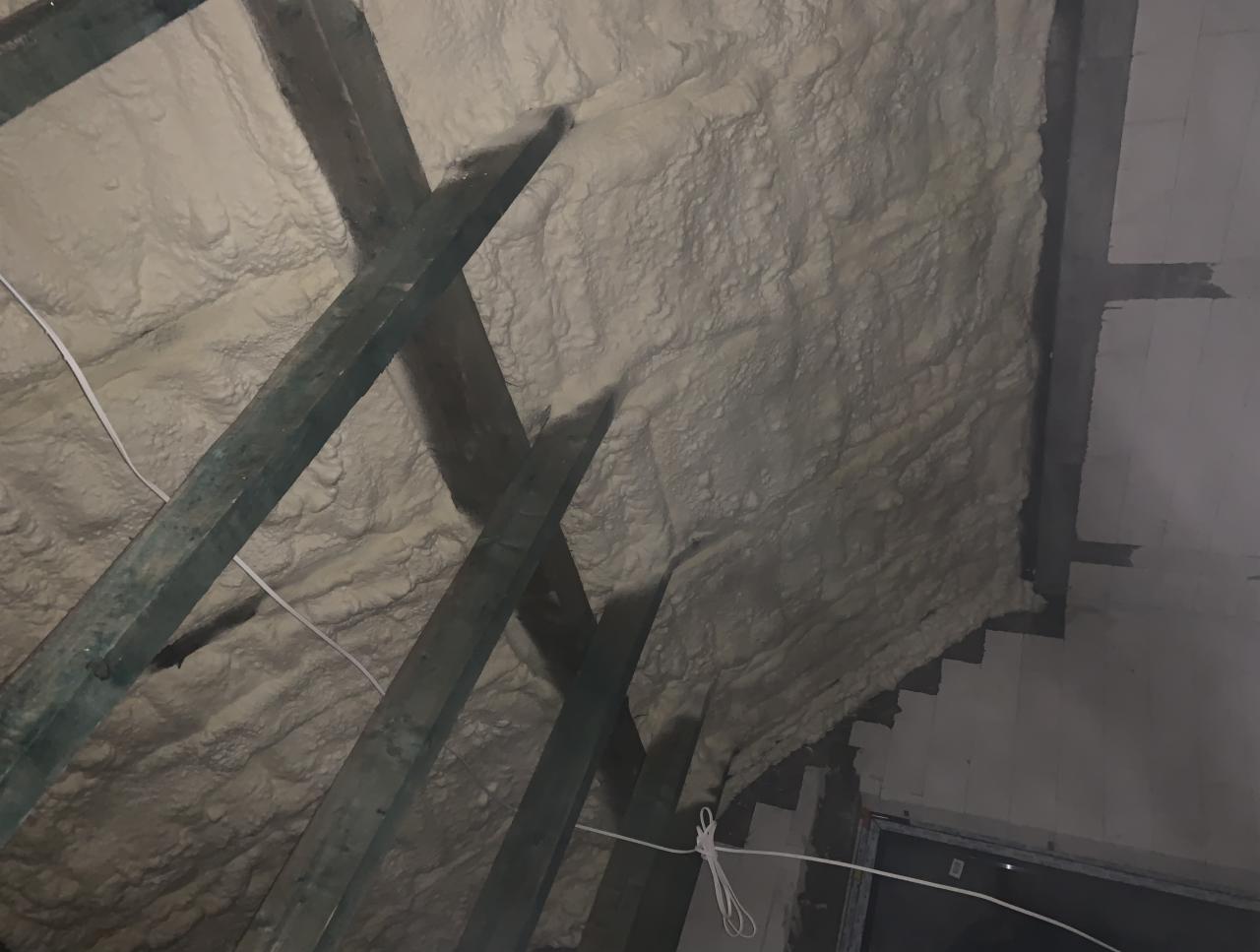 Poddasze z widoczną konstrukcją drewnianą krokwi, pokryte grubą warstwą jasnej pianki PUR, tworzącej nieregularną, porowatą powierzchnię izolacyjną.