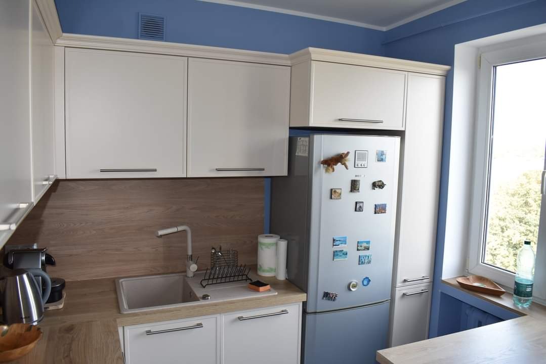 Jasna kuchnia na wymiar z drewnianym blatem i panelami, srebrna lodówka z magnesami, niebieskie ściany.