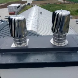 Dwa metalowe, obrotowe wywietrzniki dachowe, turbiny, zamontowane na dachu budynku z blachy trapezowej, widok z góry.