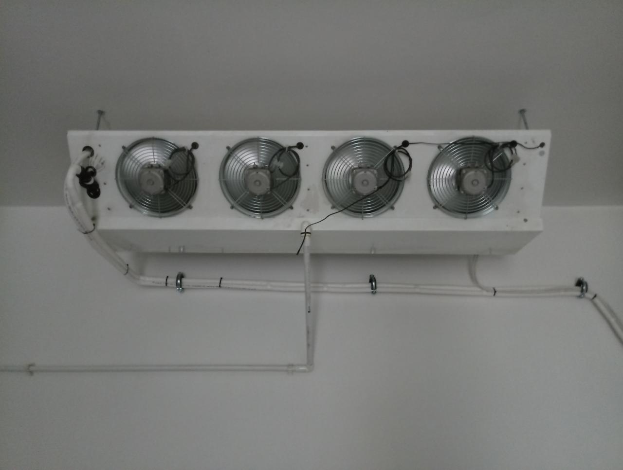 Cztery wentylatory w białej obudowie zamontowane pod sufitem, z widocznymi przewodami i rurami instalacji.