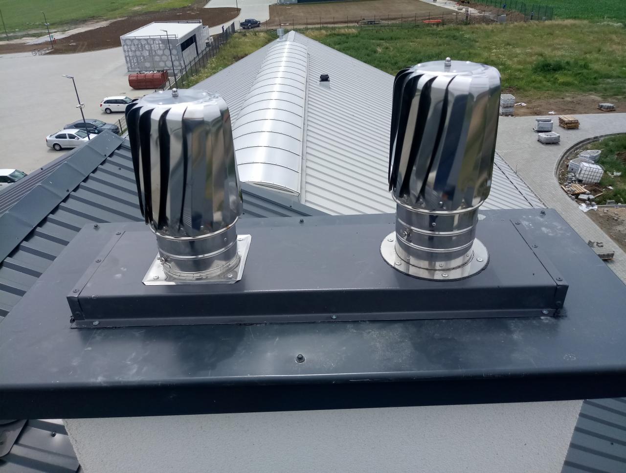 Dwa metalowe, obrotowe wywietrzniki dachowe, turbiny, zamontowane na dachu budynku z blachy trapezowej, widok z góry.