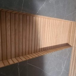 Usługi Remontowo-Budowlane Jarosław Drozd - Wnęka w ścianie wyłożona drewnianymi lamelami, przylegająca do ściany z płytek imitujących ciemny marmur.