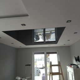 Usługi Remontowo-Budowlane Jarosław Drozd - Pokój po remoncie z pomalowanymi ścianami na szaro, z oknem balkonowym, schodami malarskimi, sufitem podwieszanym z czarnym wstawkami i oświetleniem punktowym.